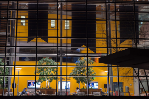 Whitman School of Management atrium. View from outside looking in at high glass windows and students seated at tables.