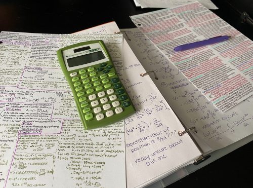 A student's study guide filled with physics notes rests on their desk.