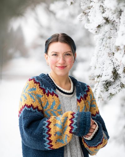 A young woman in a snowy scene wears a vibrant blue and yellow cardigan.