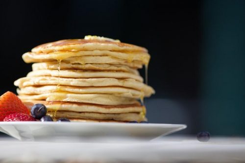 Syrup drips down a large stack of pancakes.
