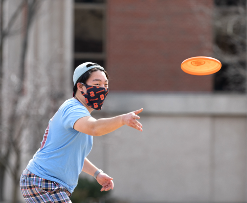 A student tosses an Orange frisbee across the Quad