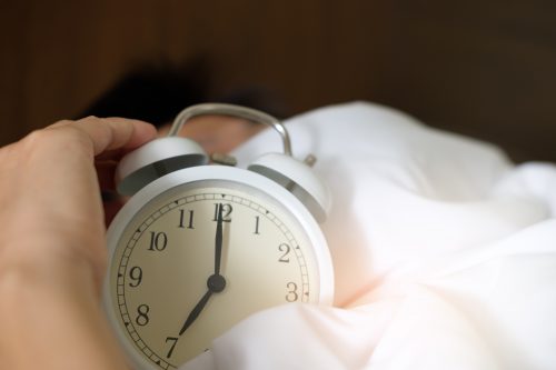 A person presses snooze on their alarm clock