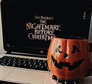 A jack-o-lantern mug in front of a laptop watching the Nightmare Before Christmas