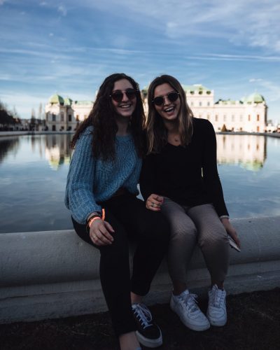 Two friends sit on a water fountain while abroad.