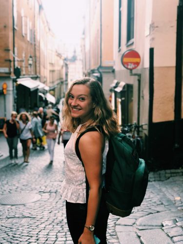 A young woman smiles over her shoulder outside of a London Tube stop.