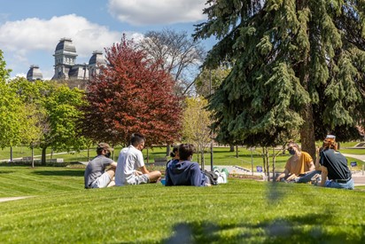 Students lounging on the hill, surrounded by trees, with the Hall of Languages in the background.