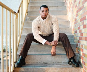 A person wearing a cream colored sweater and brown slacks posed in a stairwell.