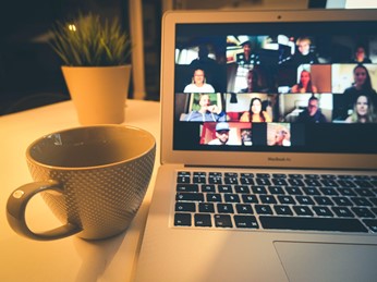 An empty mug sitting next to an open laptop with a group Zoom meeting on the screen.