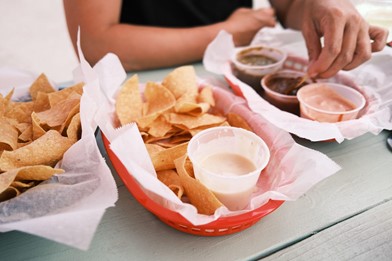 A person enjoying a basket of chips and queso with other assorted dips.