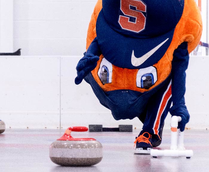 Otto the Orange throwing a curling stone at Tennity Ice Pavilion