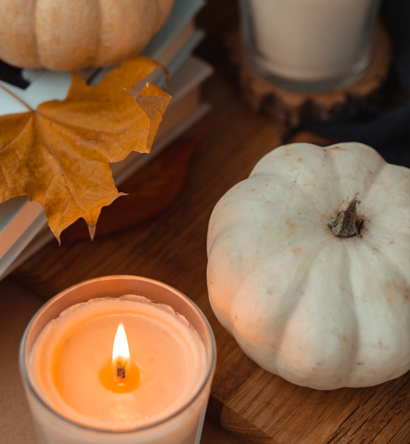 A white pumpkin sits on a table next to a lit candle.