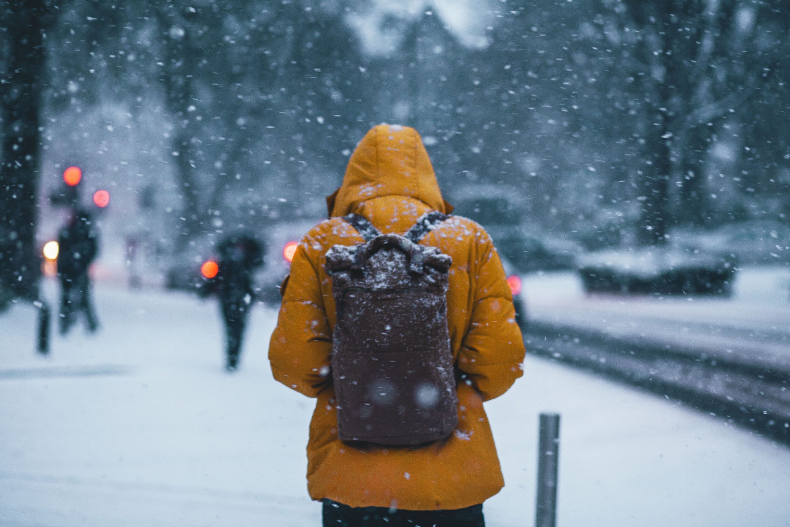 Person wearing a yellow parka and a backpack walks down a cold, snowy street.