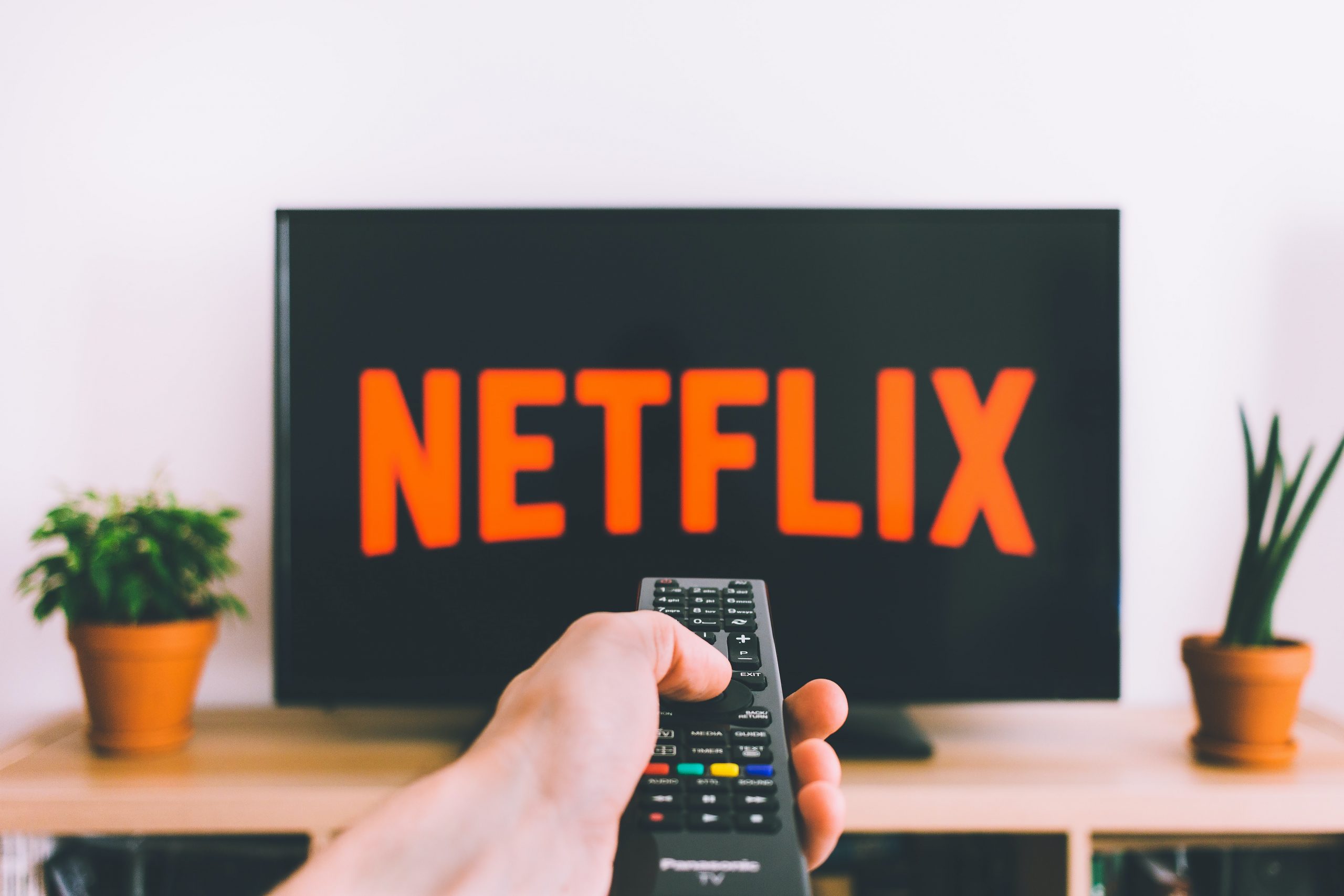 Person pointing remote at a TV that says "Netflix" on the screen