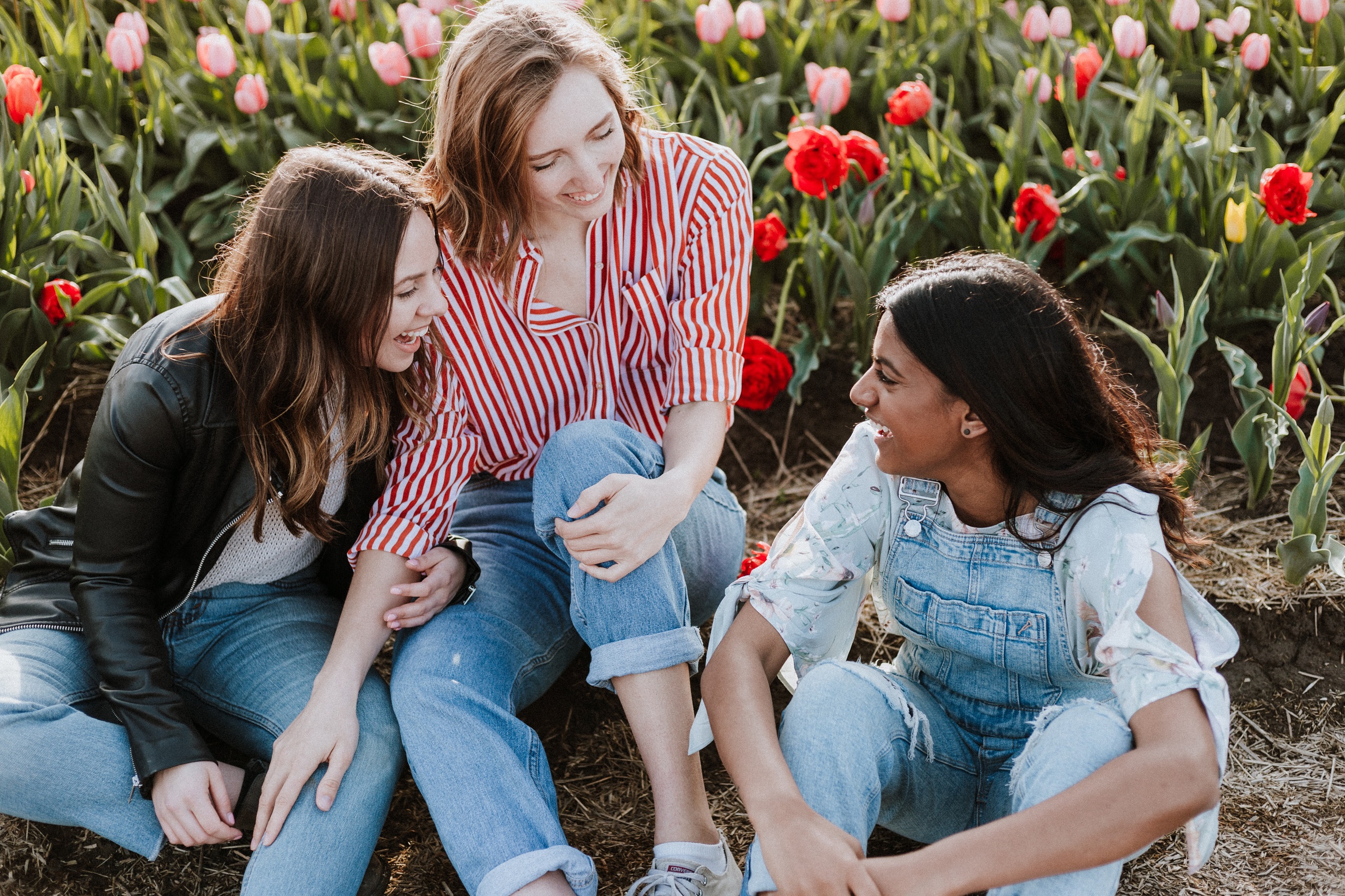 Three girls sit and laugh together in front of a bunch of tulips