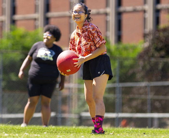 A student smiles for a photo before pitching in a game of kickball.