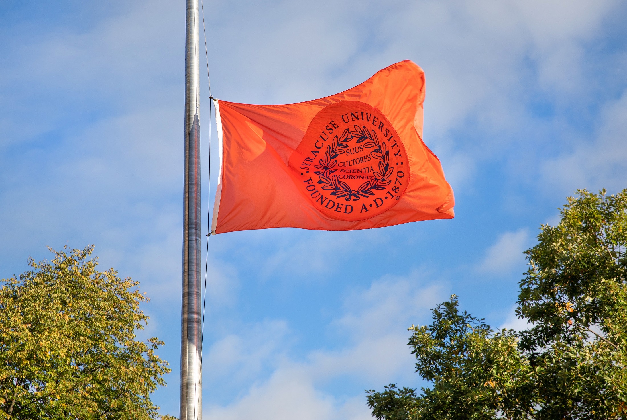 An orange flag with the Syracuse University seal flies over campus