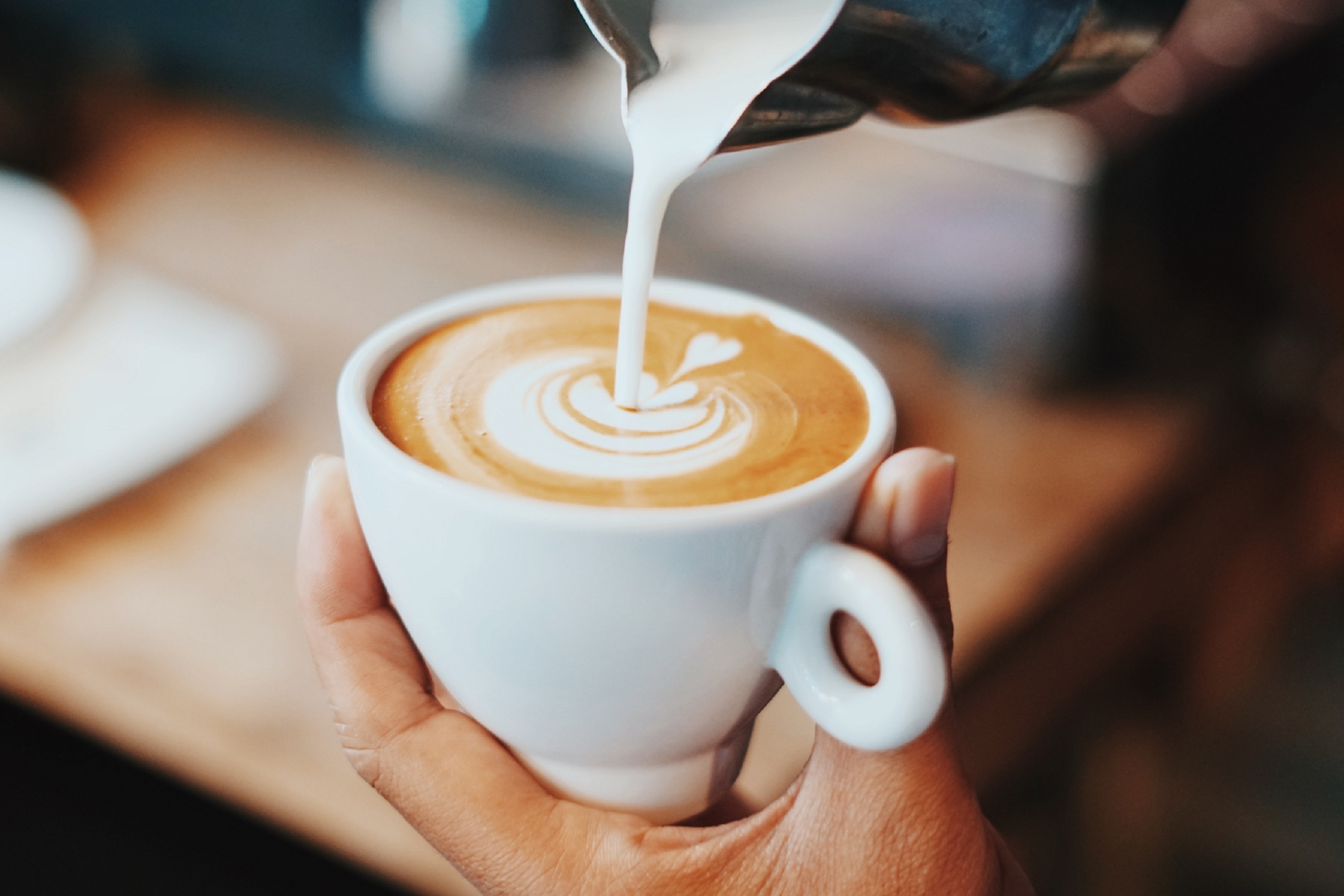 A person pours milk into coffee in a white mug
