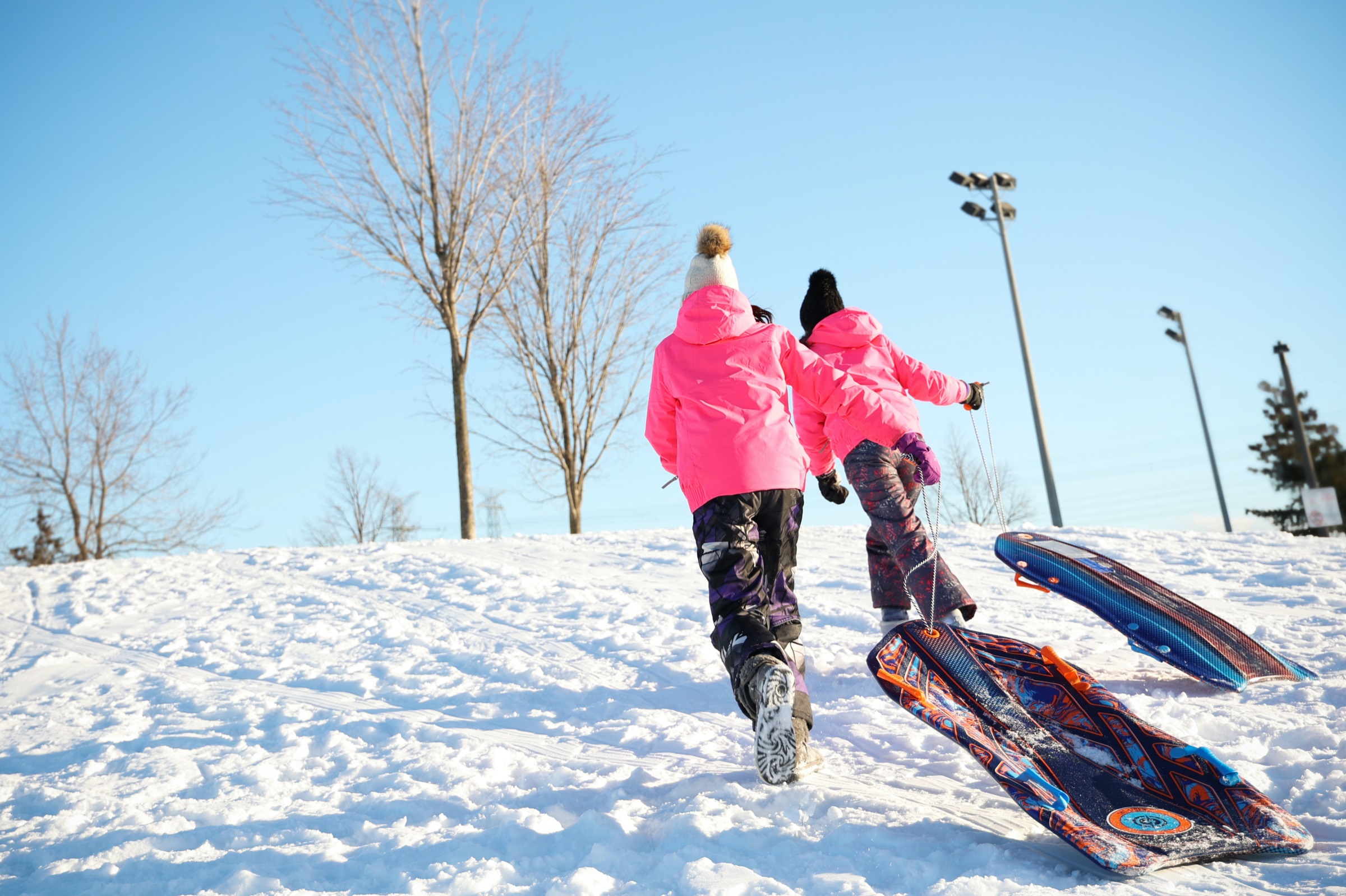 Two people run up a snowy hill with their sleds.