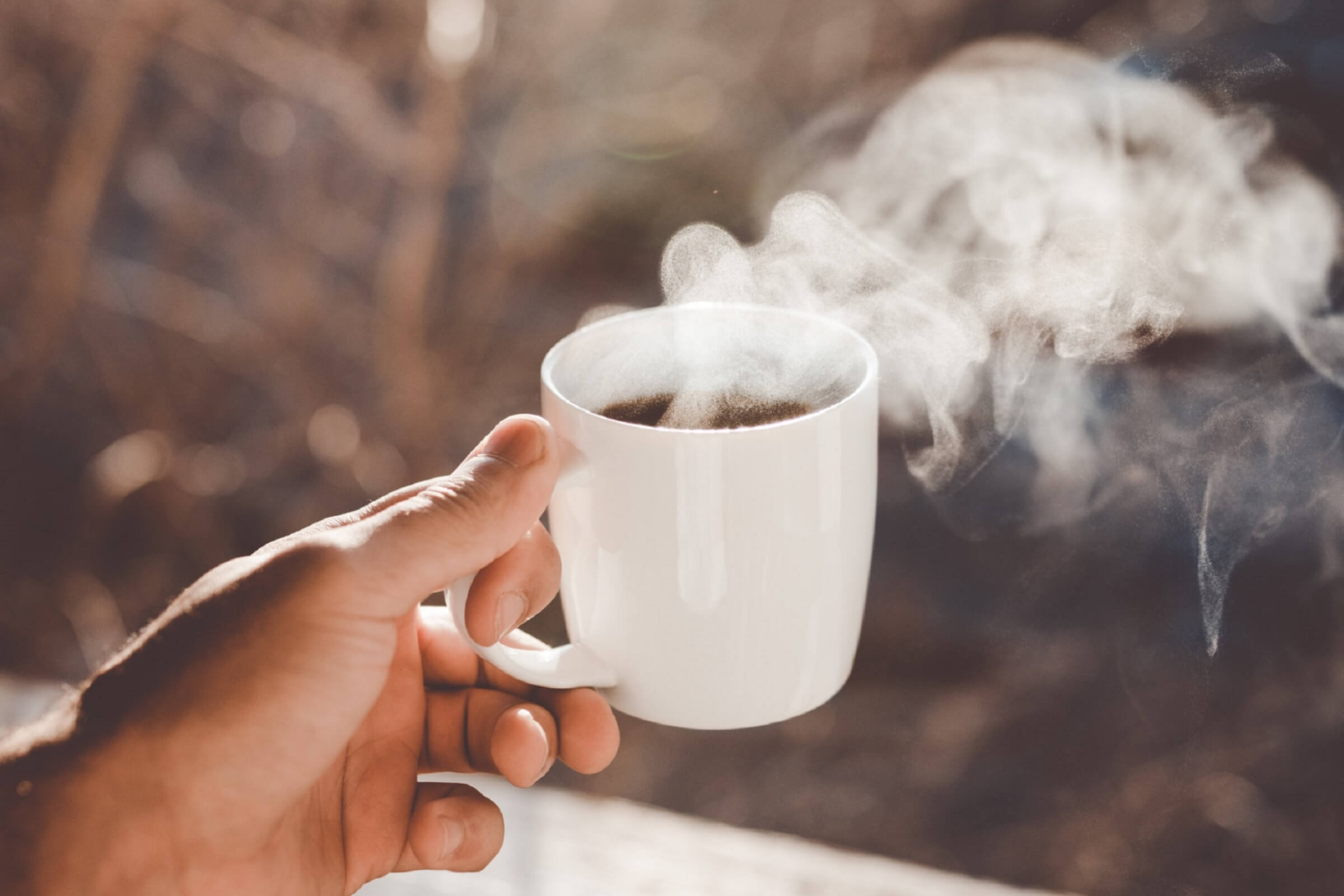 A person holds a steaming hot drink outside.
