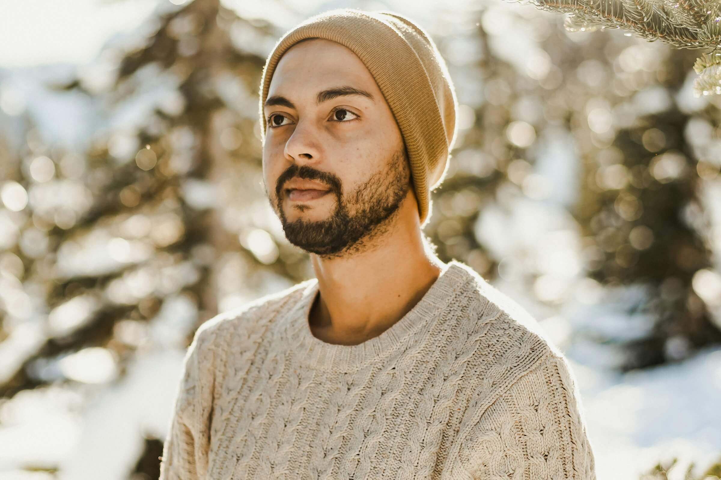 A man wears a thick sweater and a beanie outside in the snow.
