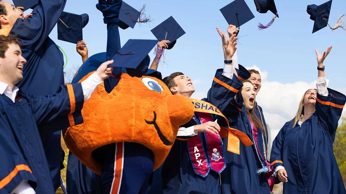 Otto and students in graduation gowns throw their graduation caps into the air.
