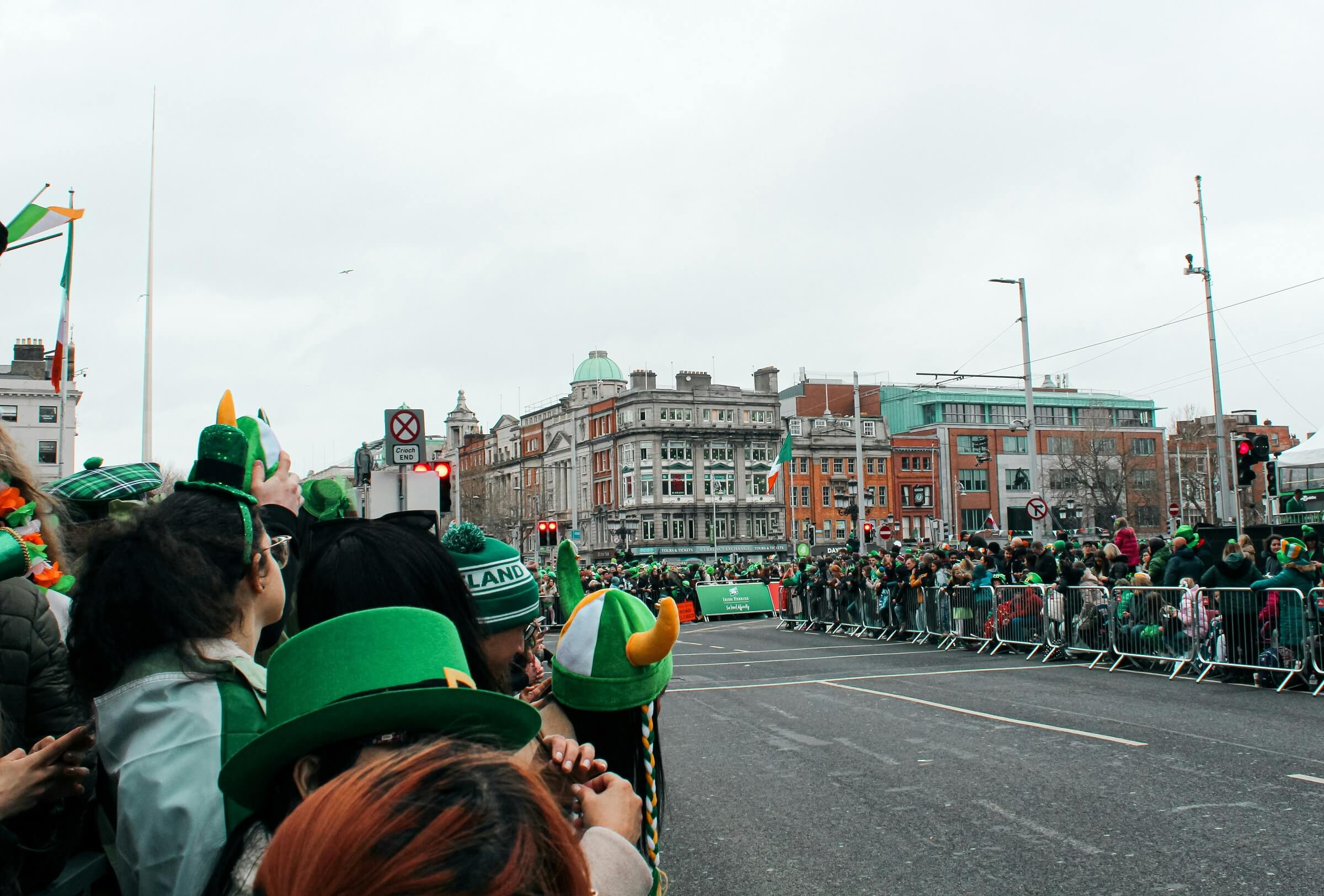 People in St. Patrick's Day gear gather along a street for a St. Patrick's Day parade.