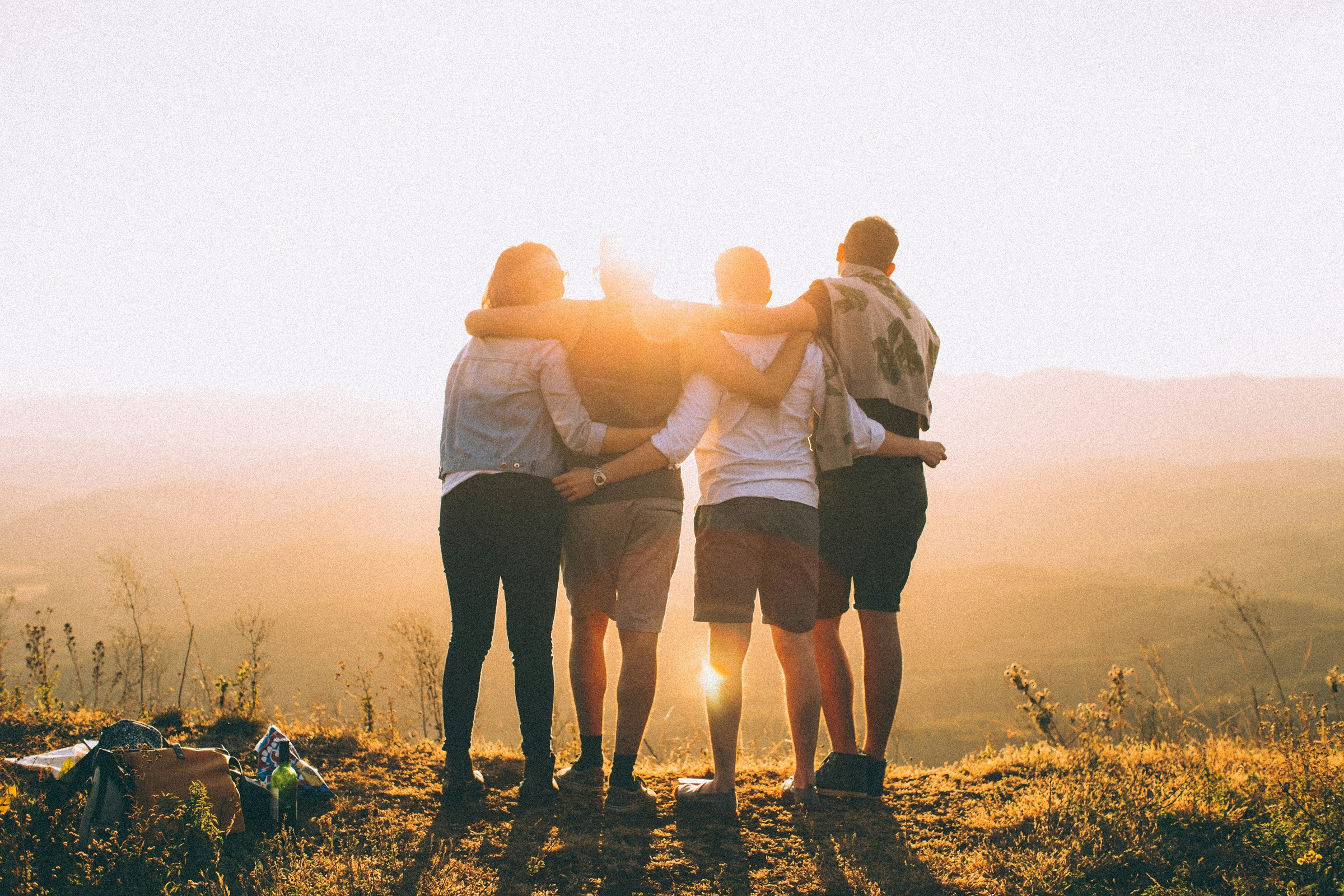 Four people stand together on the edge of a hill and look out over nearby hills as the sun set.
