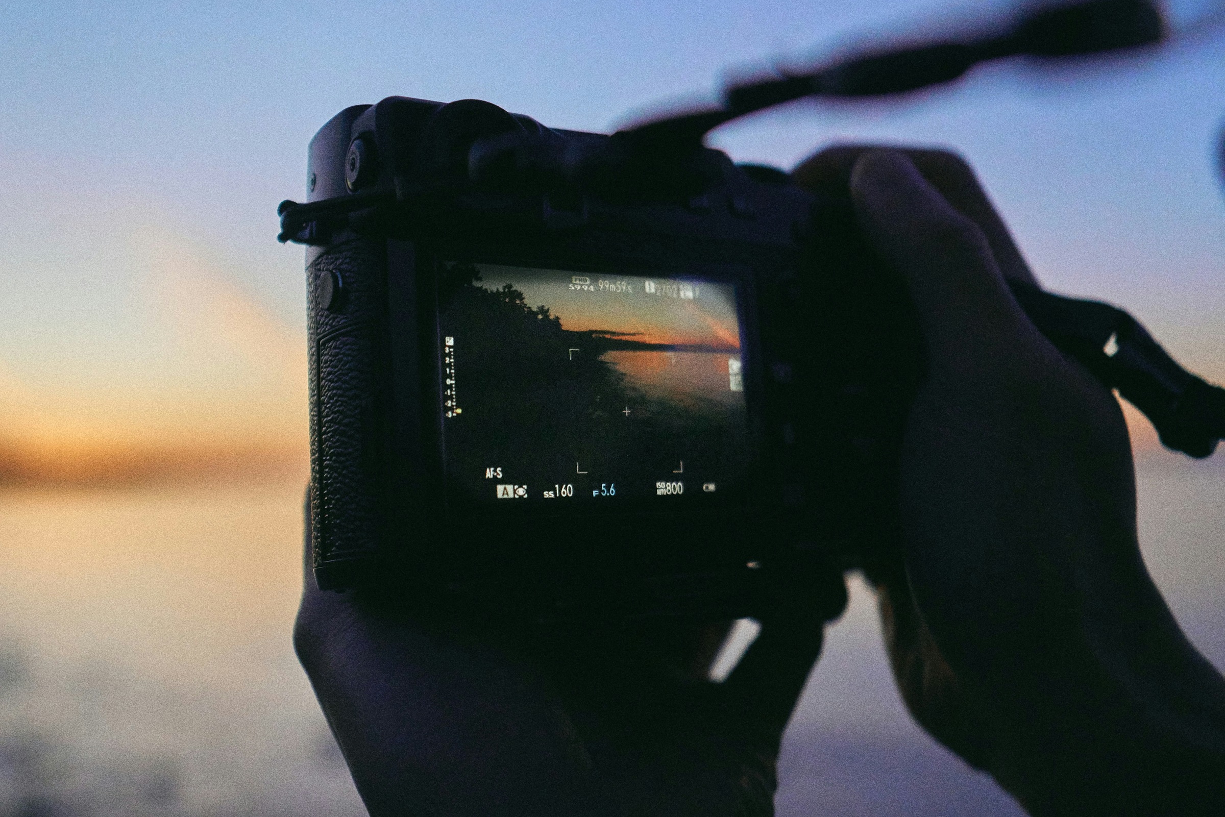 A person holds a camera up to take a photo of a sunset.