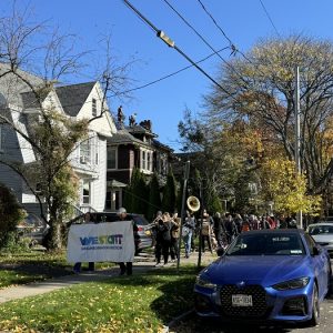 People holding a "Westcott Neighborhood Association" banner and the Second Line Syracuse brass band lead the Westcott Halloween Dog Parade