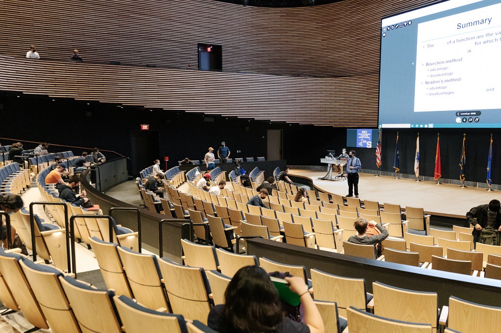 Some people sit in an auditorium on campus at a meeting.