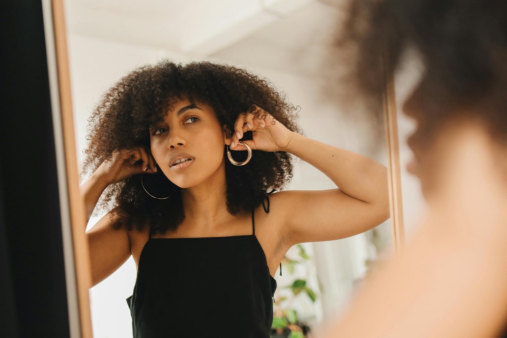 A woman tries on hoop earrings in front of a mirror,