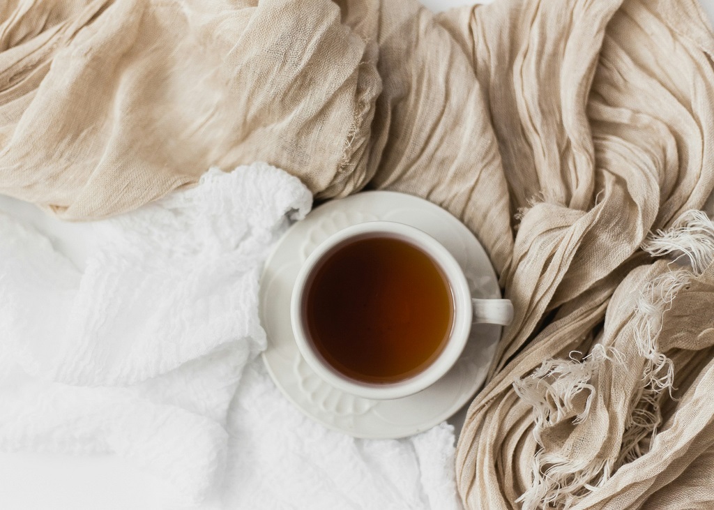 A mug of tea sits on a saucer on top of some blankets