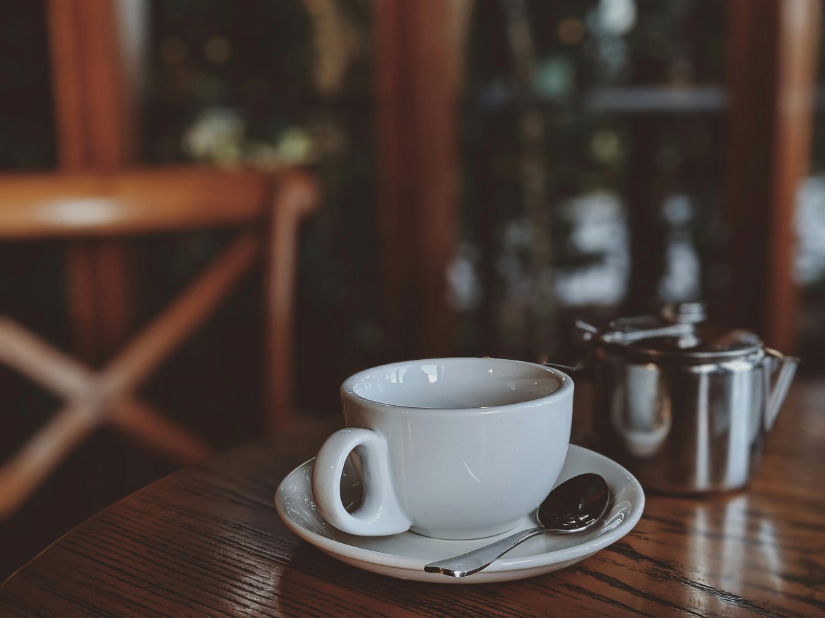 A white coffee mug and a spoon sit on a white saucer on a wooden table.