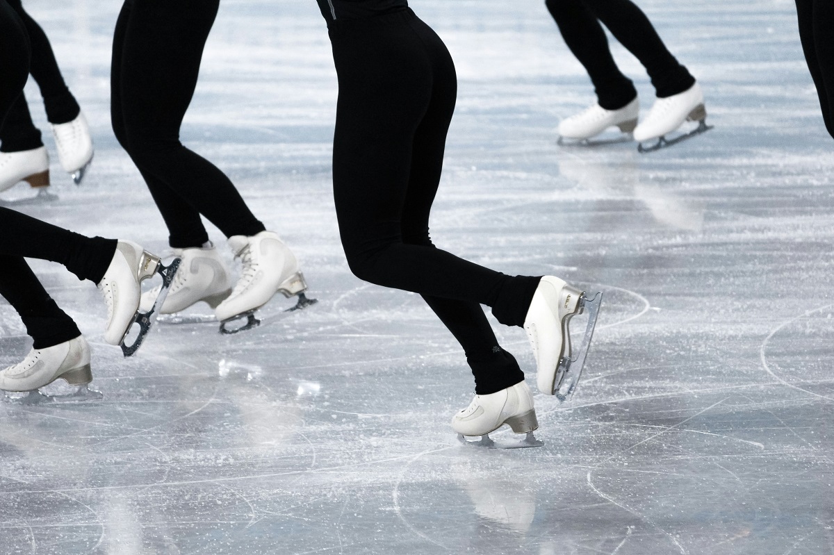 Photo of the legs and feet of five people ice skating on a rink.