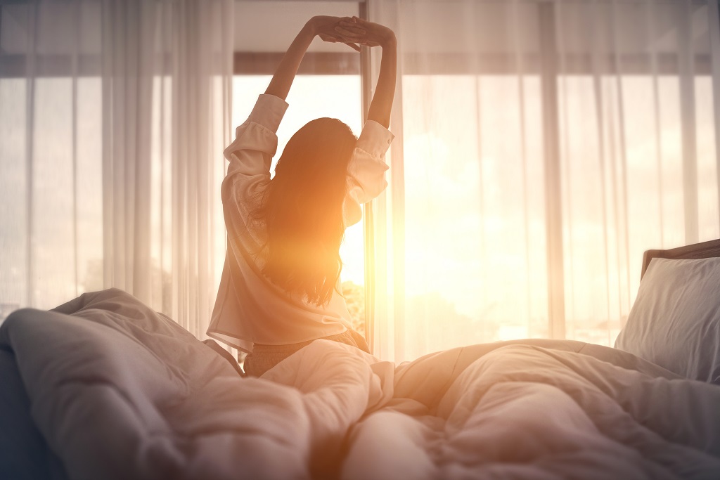 A woman stretches before getting out of bed as the sun rises.