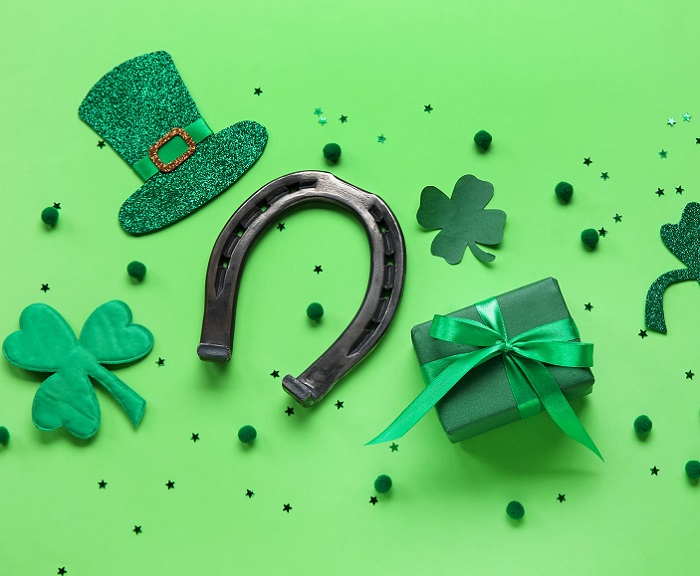 Some clovers, a green top hat, a horseshoe, a green wrapped gift and some green glitter scattered across a light green background