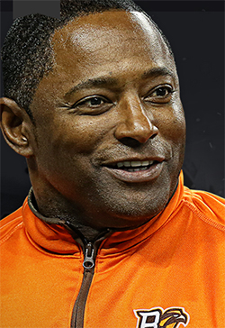 Person in orange jacket with chest logo, shown against a dark background.