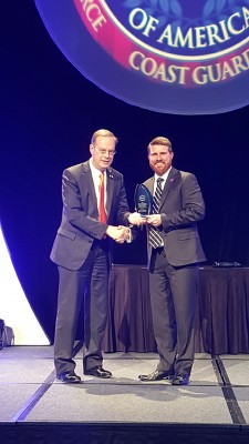 two men in suits pose with an award on a stage