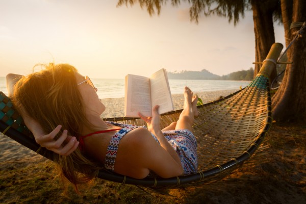 Young lady reading a book in hammock on a beach at sunset