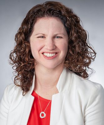 Photo of a smiling woman with curly hair wearing a red blouse with a white jacket
