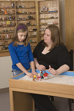 A counselor works with a child at a sand table. 