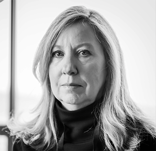 Black‑and‑white portrait of a person with long, wavy hair wearing a dark turtleneck, seated indoors near a window.