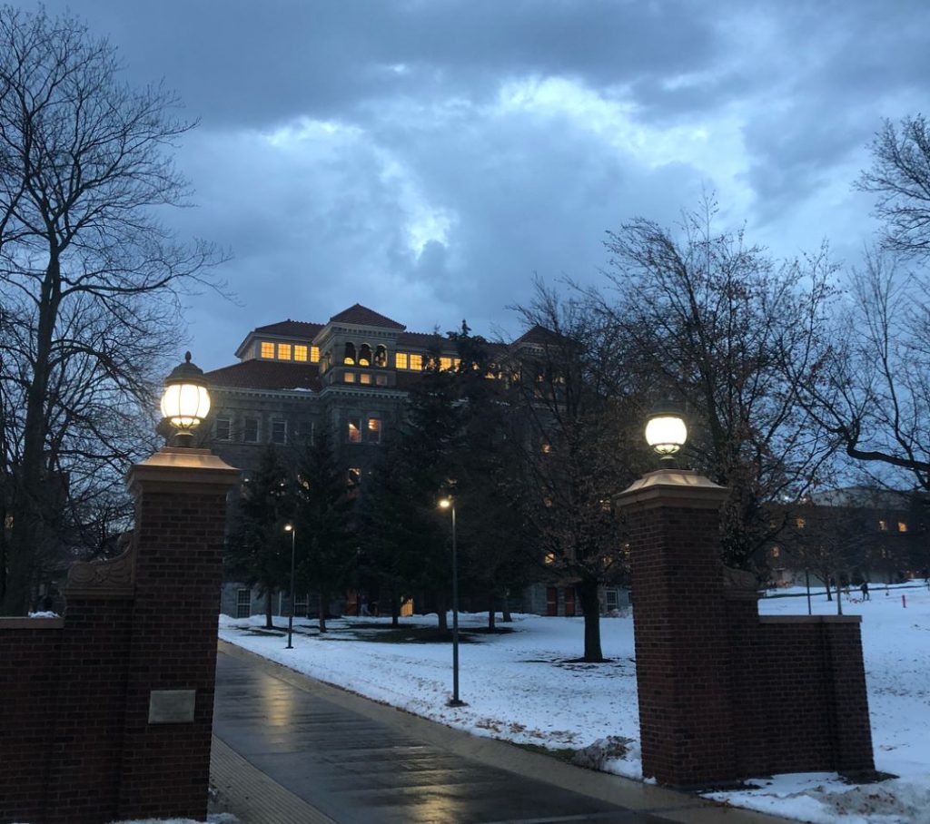 campus walkway in front of snow-covered grass and building at night