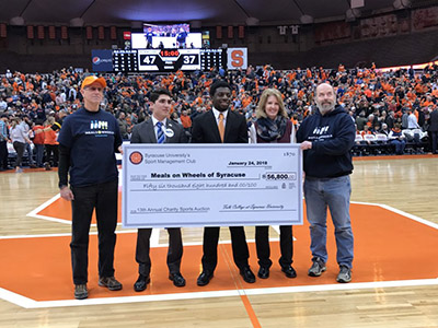 five people holding a big check on the floor of the Carrier Dome