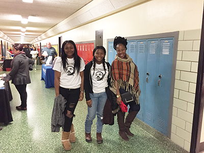Three girls walking down school hallway, two wearing MLK T-shirts
