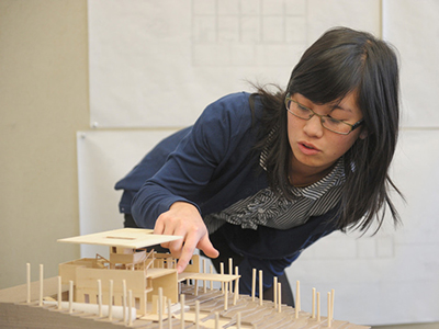 Asian student pointing out feature on model of building