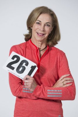 A runner poses for a photo while holding up her bib number 261.