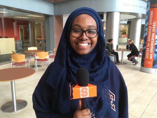 Ghufran Salih holds cuse cast microphone while standing in sci tech building lobby