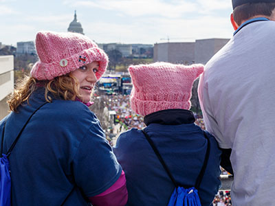 Three people, two in pussy hats, looking out over the March for Our Lives