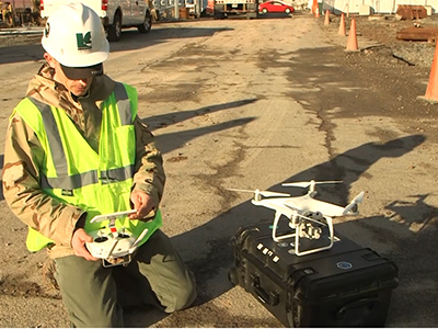 Man in hard hat with controller kneeling next to drone